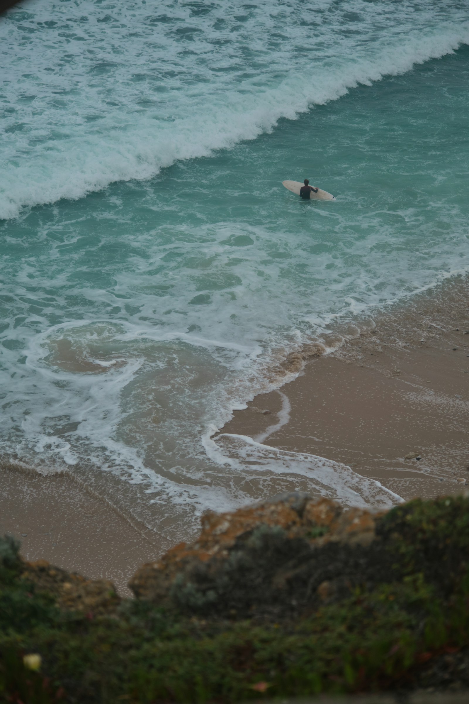 Surfer entering the ocean below the cliffs at Ericeira, Portugal