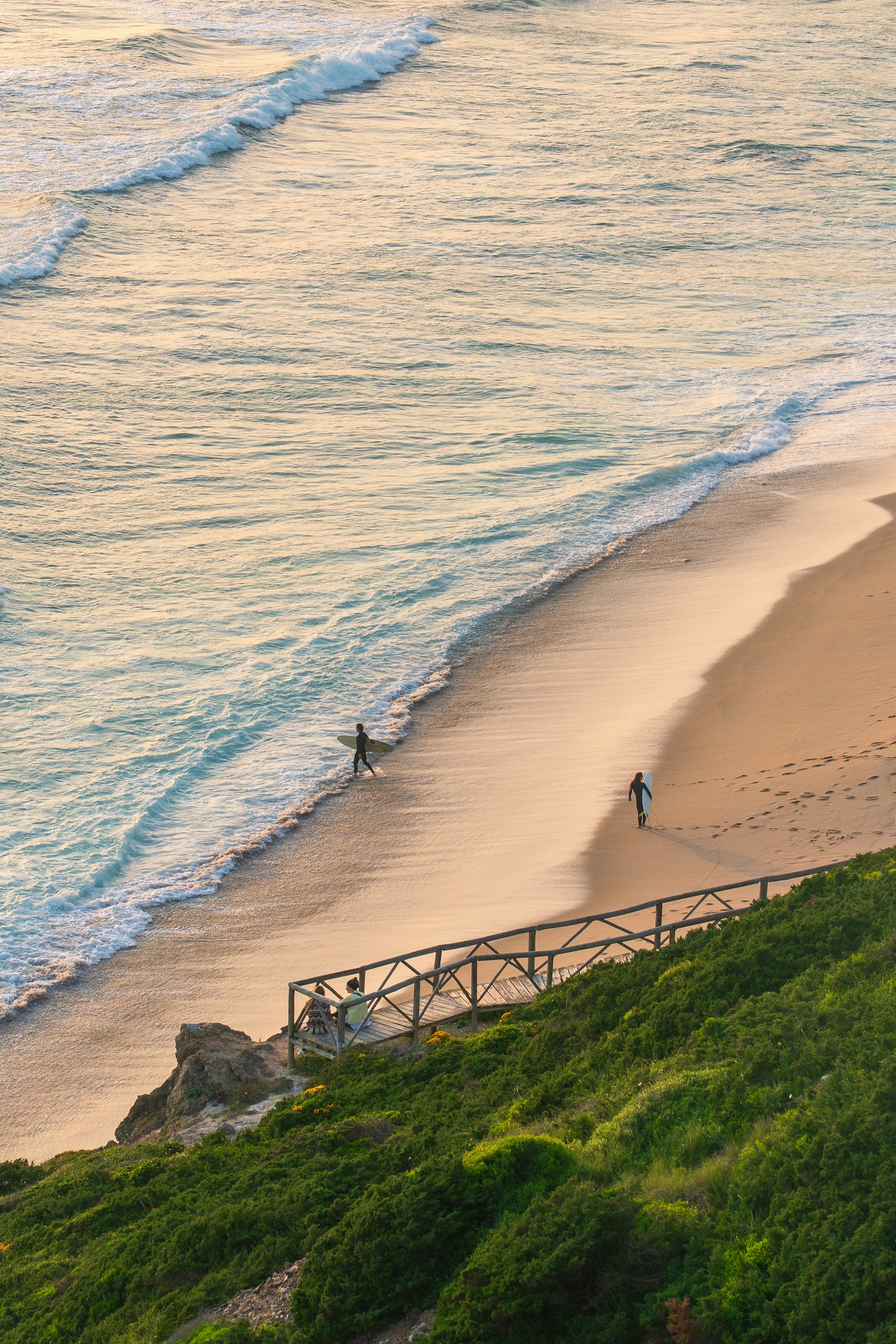 Surfers walking along an Ericeira beach at sunset